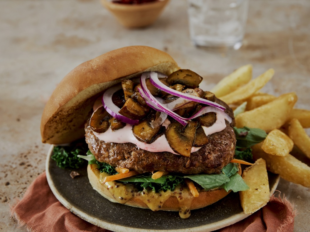 Saftig burger med sopp, rødløk og grønt på en tallerken, servert med grove pommes frites