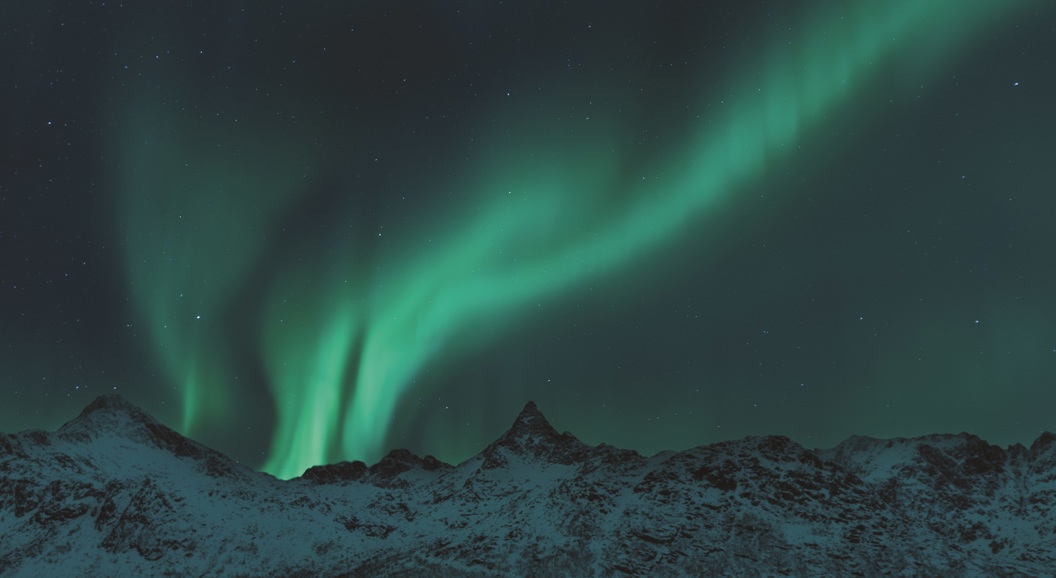 Nordlys over snødekte fjell i nattelandsskap, klare stjerner i mørk himmel