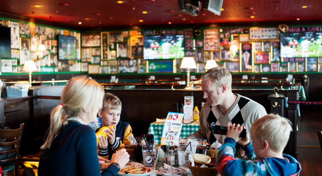 Family dining at a sports-themed restaurant with memorabilia-covered walls, children enjoying food and drinks at a checkered table