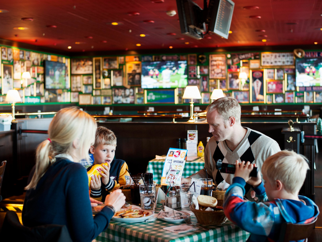 Family dining at a sports-themed restaurant with memorabilia-covered walls, children enjoying food and drinks at a checkered table