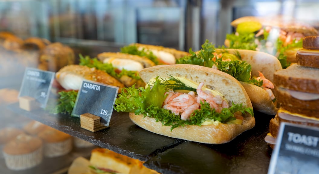 Fresh seafood sandwich with shrimp, lettuce, and herbs on ciabatta bread displayed in a deli case