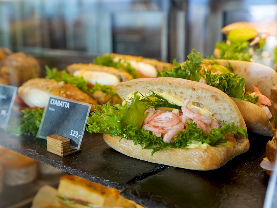 Fresh seafood sandwich with shrimp, lettuce, and herbs on ciabatta bread displayed in a deli case