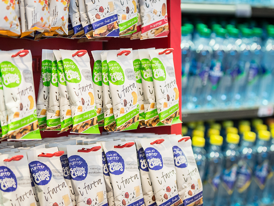 Snack display in a supermarket with shelves featuring various packaged chips and bottled water in the background