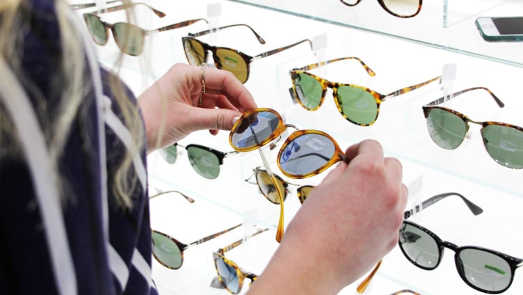 Person browsing a display of designer sunglasses in a store, examining tortoiseshell frames under bright lighting