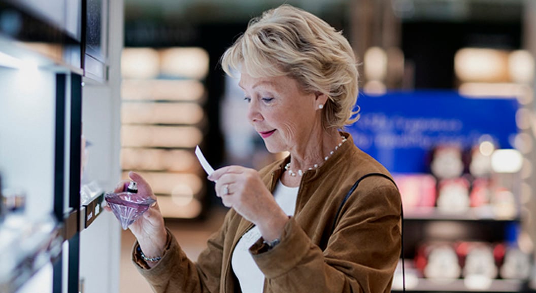 Senior woman testing perfume in a retail store, examining fragrance options