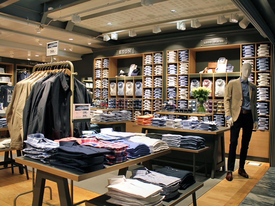 Herreklærbutikkens interiør med pent stablede skjorter, jakker på et stativ, og en mannequin iført en beige blazer, som viser frem en stilfull og organisert butikkvisning