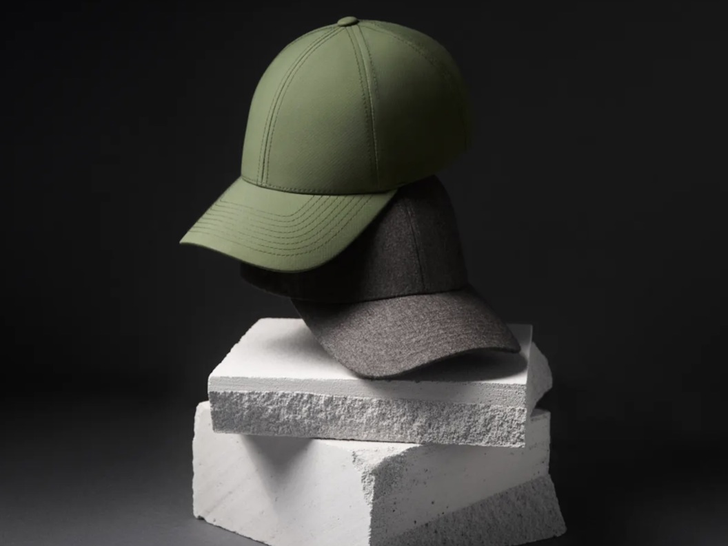Two stylish caps, one green and one gray, are placed on stacked white concrete blocks with a dark background