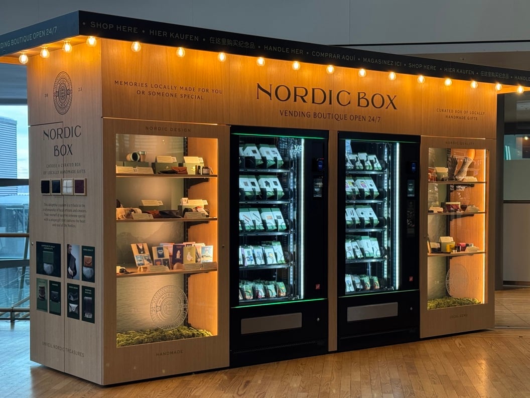 Nordic Box vending boutique in airport, offering locally crafted gifts. Features illuminated display shelves and vending machines stocked with assorted items. Open 24/7