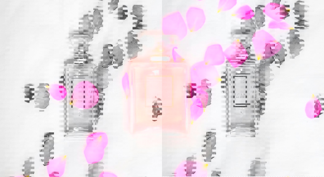 Rosa parfymeflaske omgitt av rosa roseblader på en hvit bakgrunn, som skaper en elegant og feminin estetikk