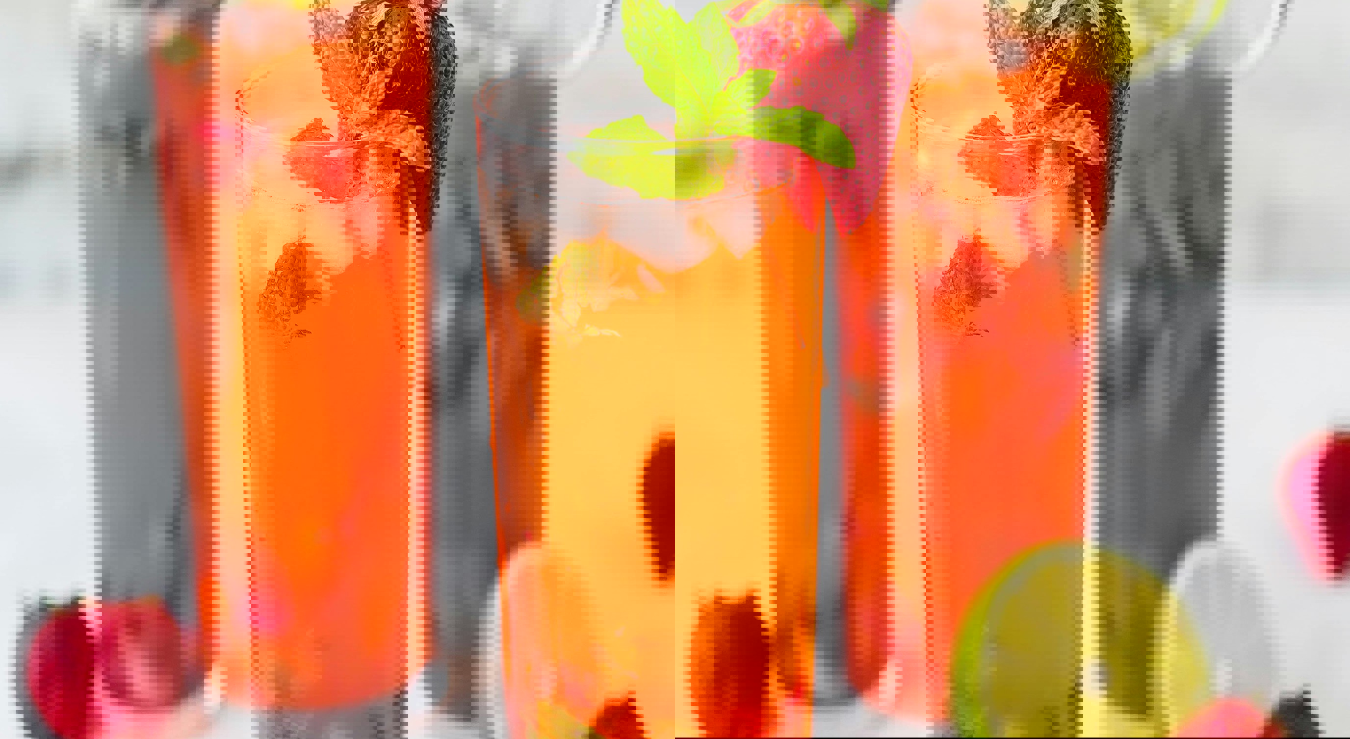 Three tall glasses of strawberry mojito cocktails garnished with fresh strawberries, mint leaves, and lime slices, surrounded by additional strawberries and lime wedges on a light background