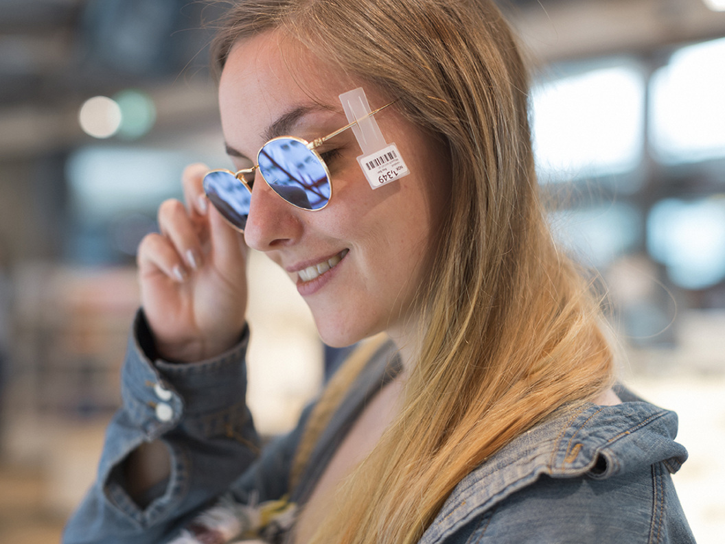 Kvinne smiler mens hun prøver blå solbriller innendørs, med prislappen fortsatt festet