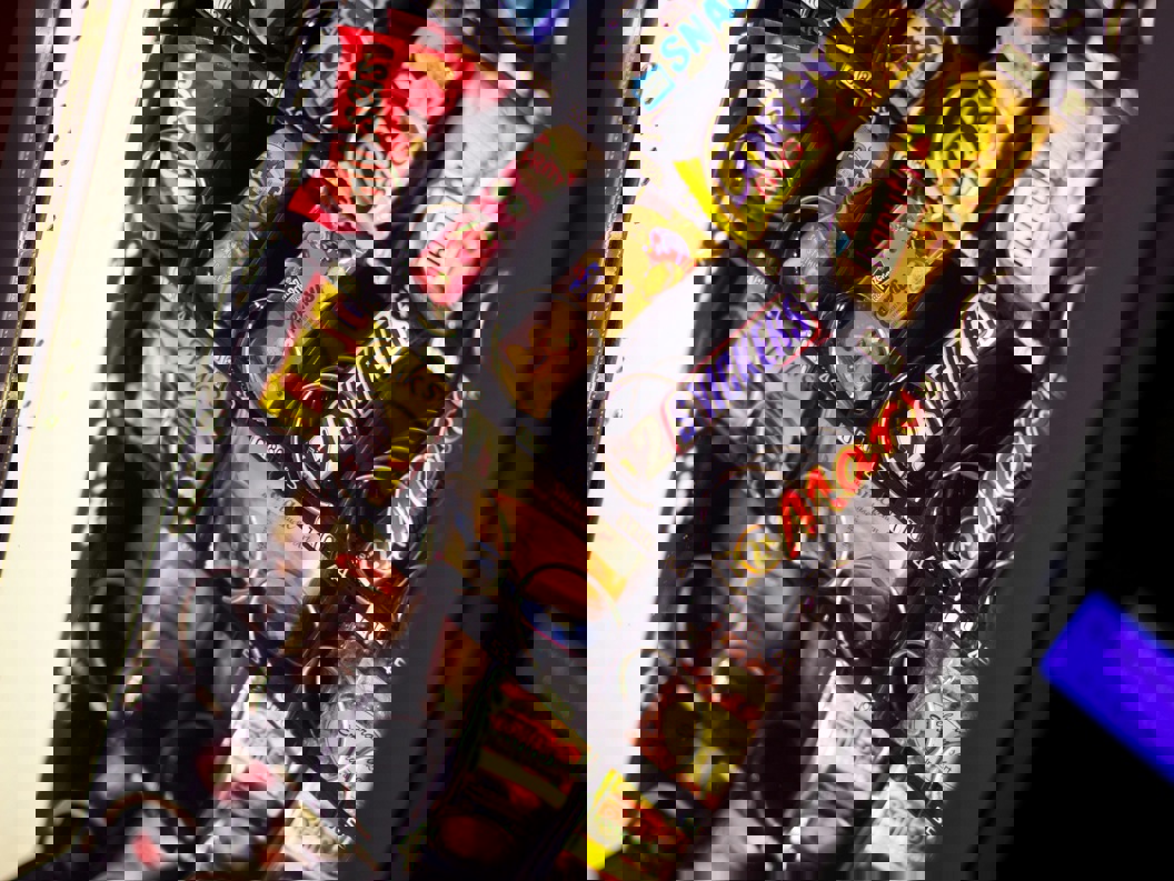 Automat fylt med assorterte snacks og sjokoladebarer, inkludert populære merker, med opplyst valgpanel