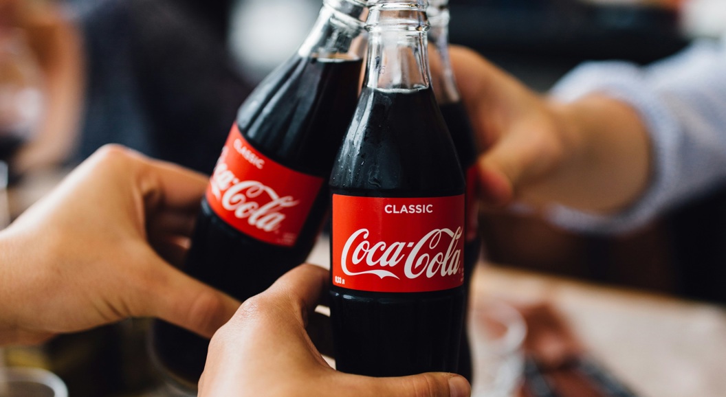 Tre personer skåler med Coca-Cola-flasker i en avslappet setting, og fremhever sosial tilknytning og glede