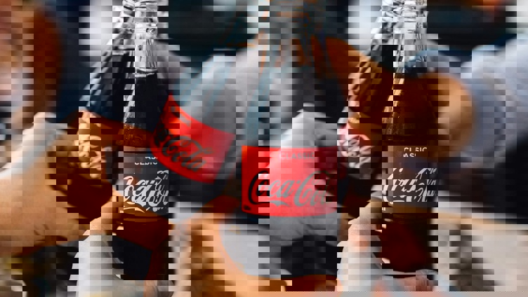 Tre personer som skåler med Coca-Cola-flasker i en avslappet setting, som fremhever sosial tilknytning og glede