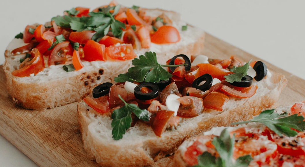 Tre skiver surdeigsbrød med kremost, cherrytomater, sorte oliven og fersk persille på en treplate