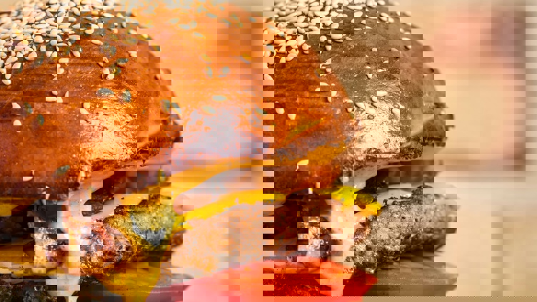 Juicy cheeseburger with lettuce, tomato, onion, and melted cheese on a sesame seed bun, secured with a skewer, set against a brick background