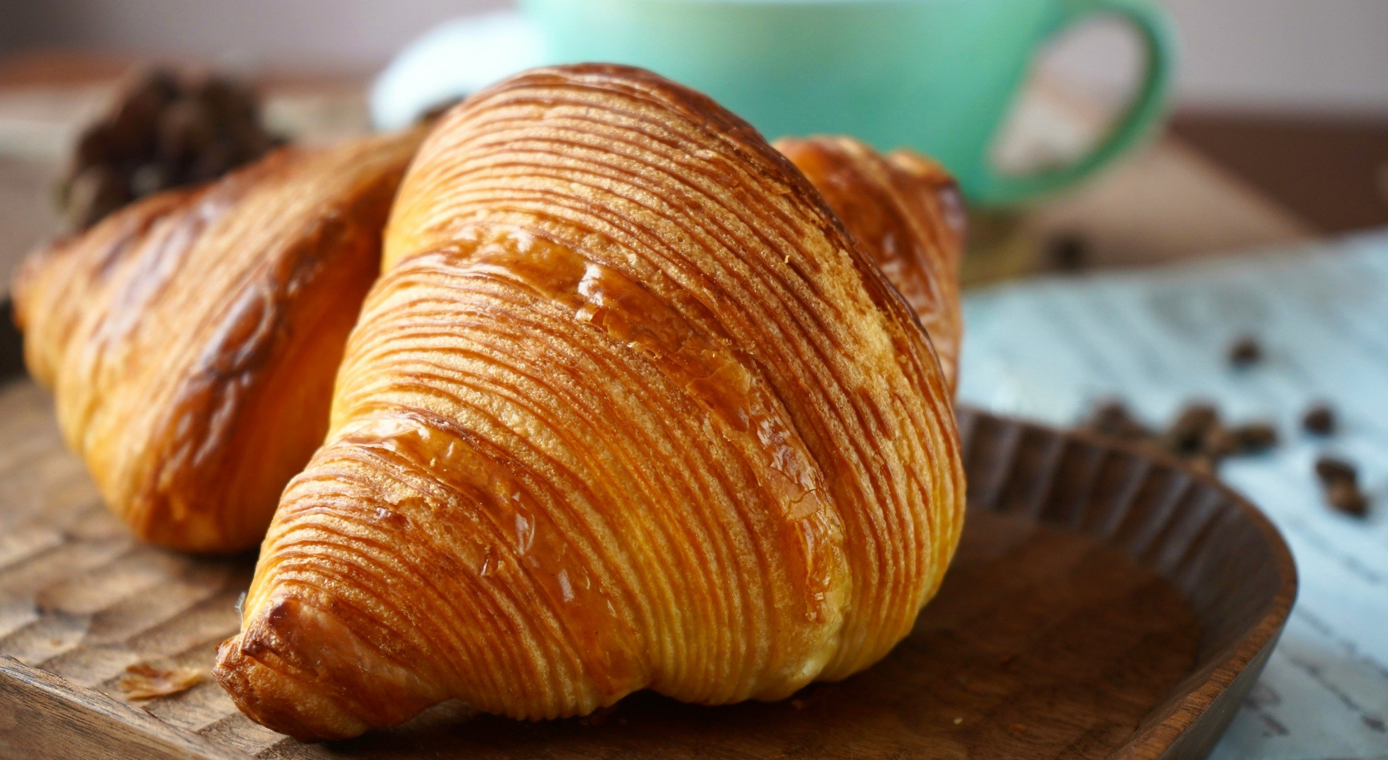 Nystekte croissanter på et trebord med en turkis kaffekopp i bakgrunnen