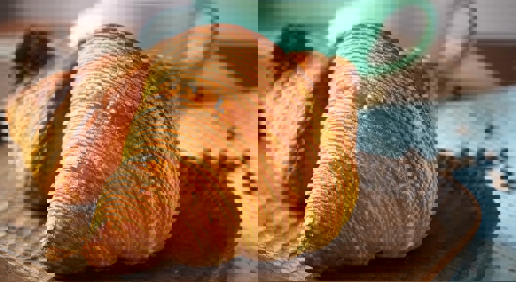 Golden, flaky croissants on a wooden plate with a teal coffee cup in the background