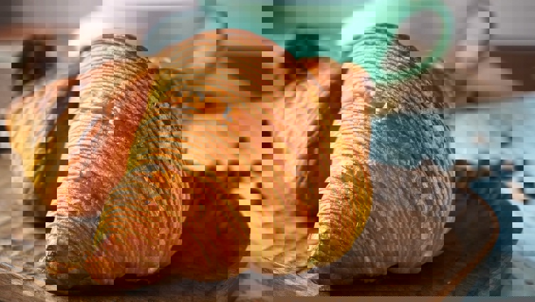 Nystekte croissanter på et trebret med en turkis kaffekopp i bakgrunnen
