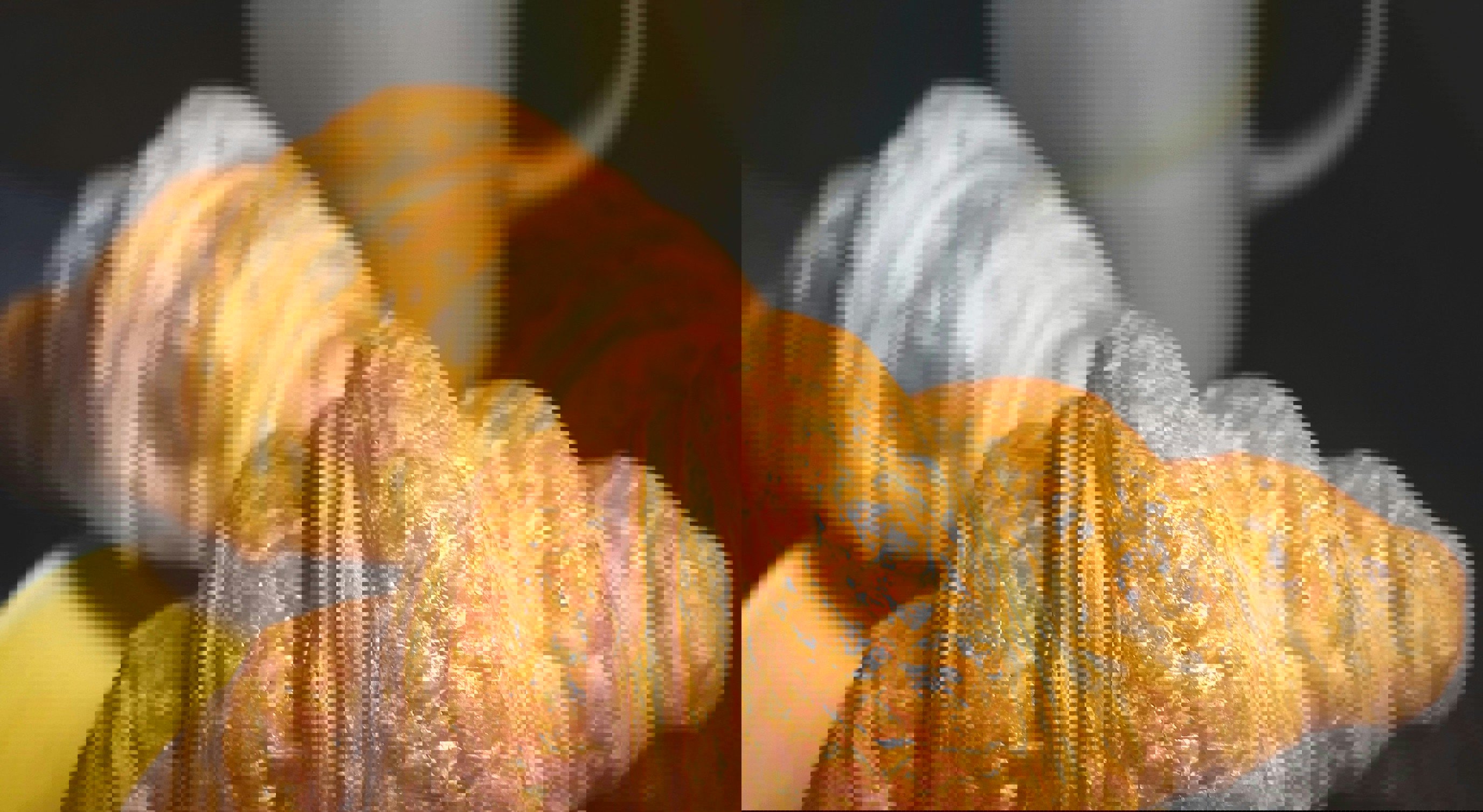 To gyldne croissanter på en gul tallerken ved siden av en kopp kaffe, plassert på et mørkt trebord