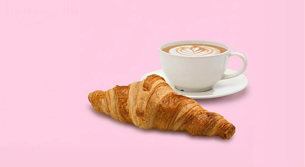 Kopp med kaffe og en croissant ved siden av.