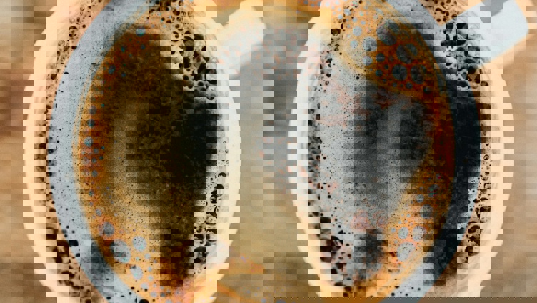 Topp utsikt over en dampende svart kaffe i en hvit kopp på et rustikt trebord