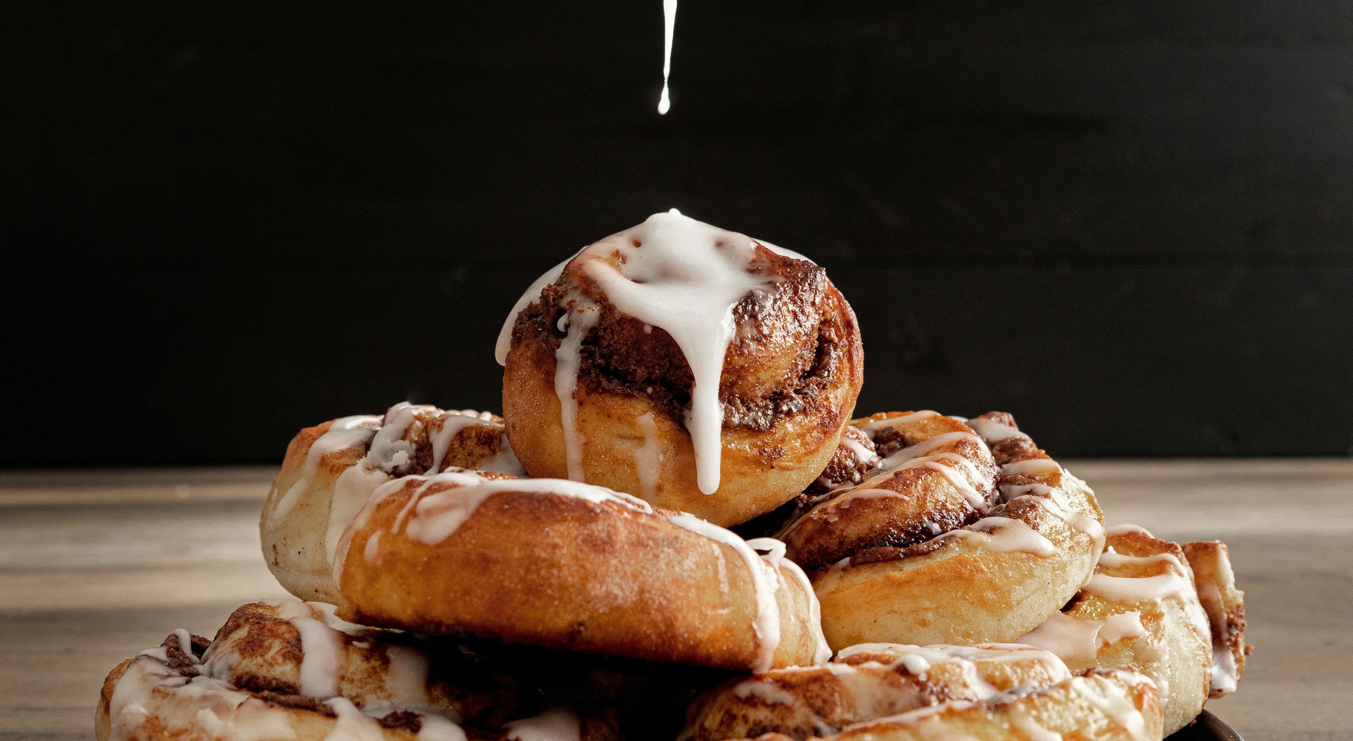 Drizzling icing over freshly baked cinnamon rolls stacked on a black plate