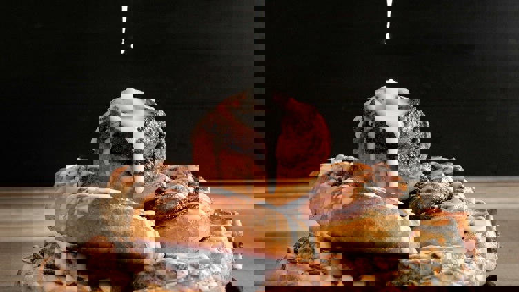 A stack of freshly baked cinnamon rolls with icing being drizzled from a spoon onto the top roll, set against a dark background, resting on a wooden table