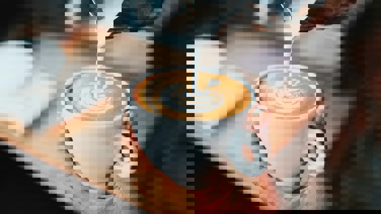 Barista pouring latte art into a cup of coffee, creating a heart shape design, held in a person's hand