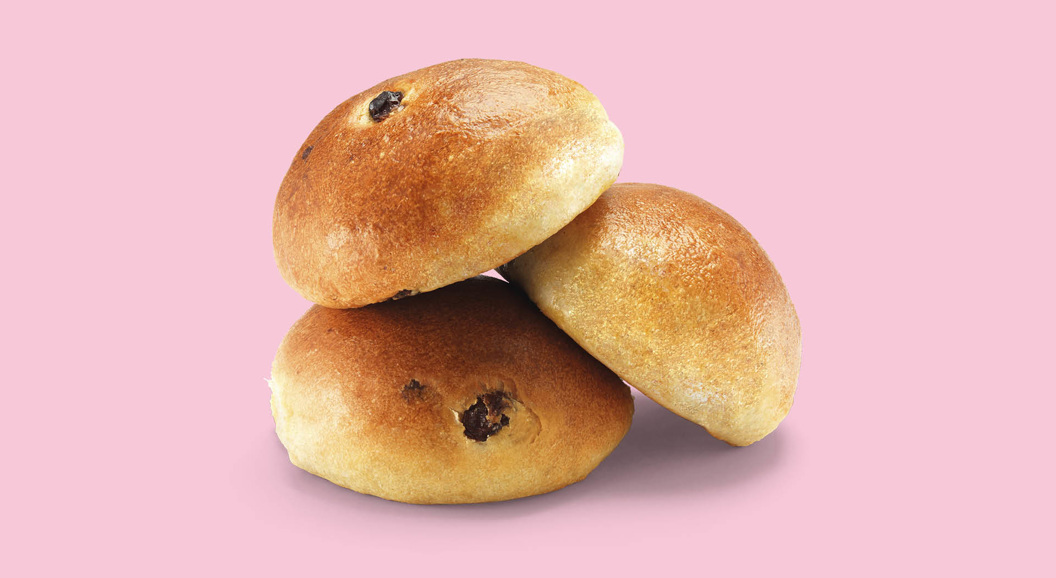 Tre rosinboller stablet på rosa bakgrunn.