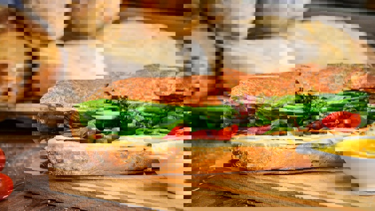 Fersk sandwich med salat, tomat, ost på en sprø baguette, servert på et trebrett med en side av sennep, med brød i bakgrunnen