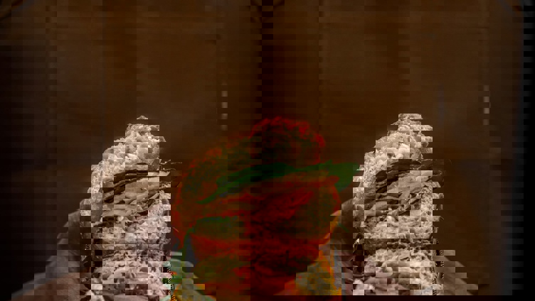 Artisanal sandwich with fresh ingredients held in hands wearing a brown apron