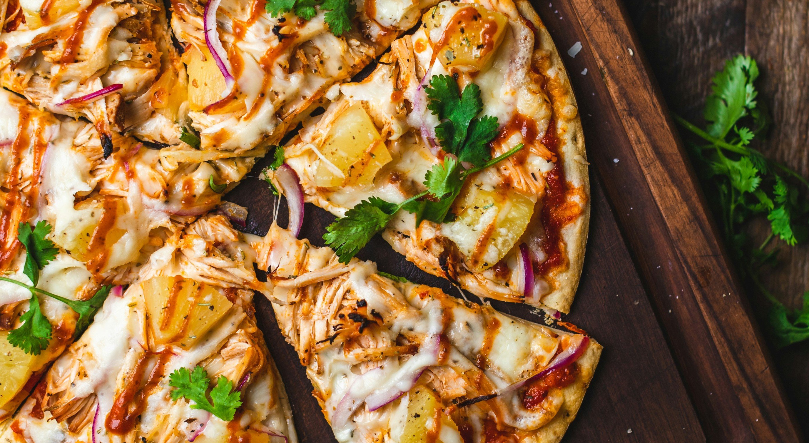 Gourmet barbecue chicken pizza with pineapple, red onion, cilantro, and melted cheese on a rustic wooden board