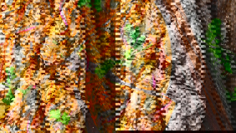 Gourmet barbecue chicken pizza with pineapple, red onion, cilantro, and melted cheese on a rustic wooden board