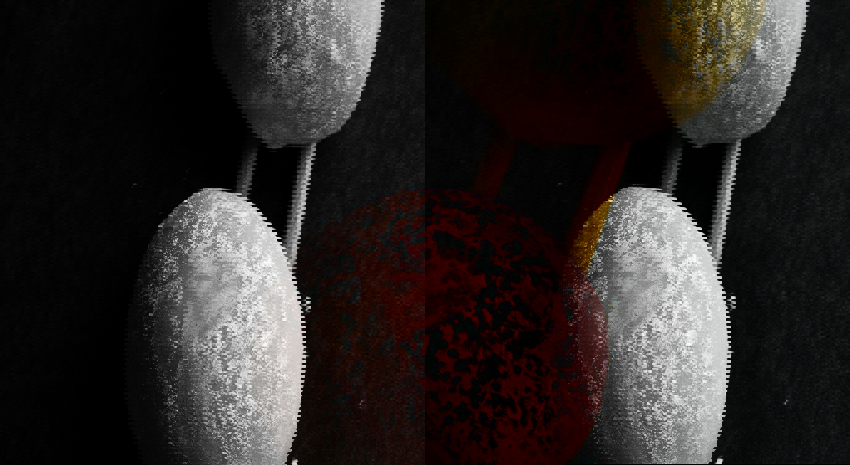 To mochi-boller, en rosa og en gul, plassert på trepinner mot en svart bakgrunn