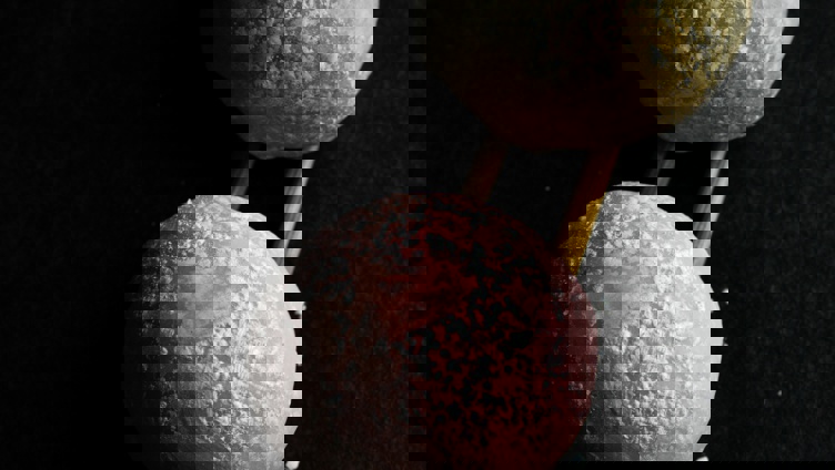 To mochi-boller, en rosa og en gul, plassert på trepinner mot en svart bakgrunn