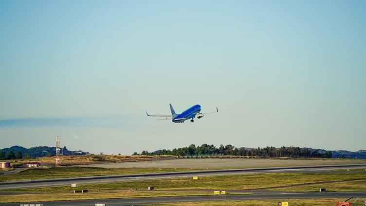 Fly som tar av fra rullebane på flyplass, klar blå himmel i bakgrunnen.
