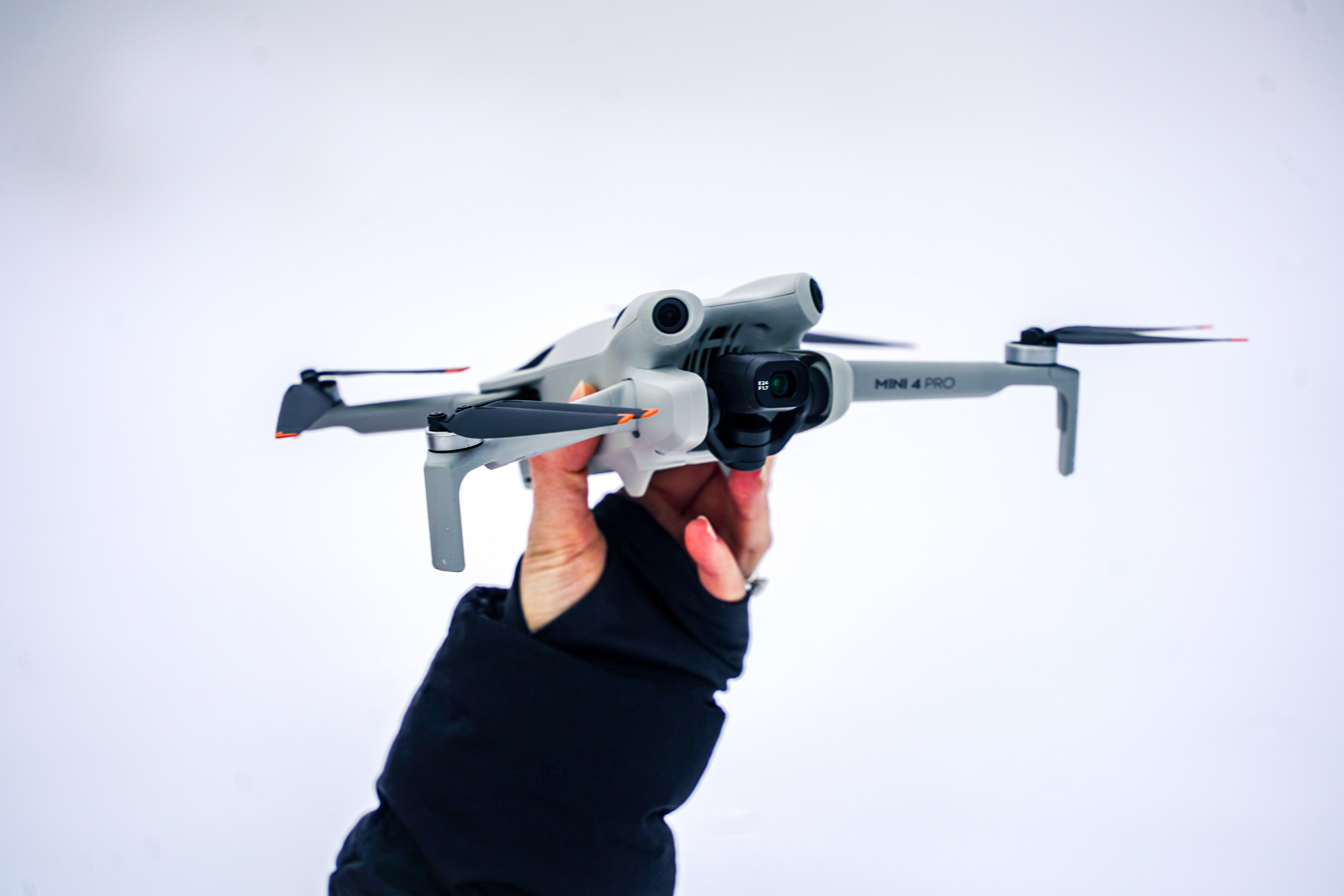 Hand holding a gray Mini 4 Pro drone against a white background, ready for takeoff.