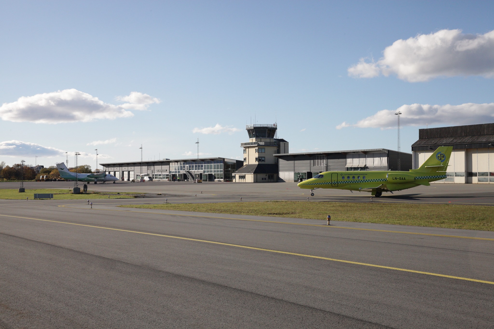 To fly på flyplassen i klårt vêr med flytårn og hangarar i bakgrunnen.
