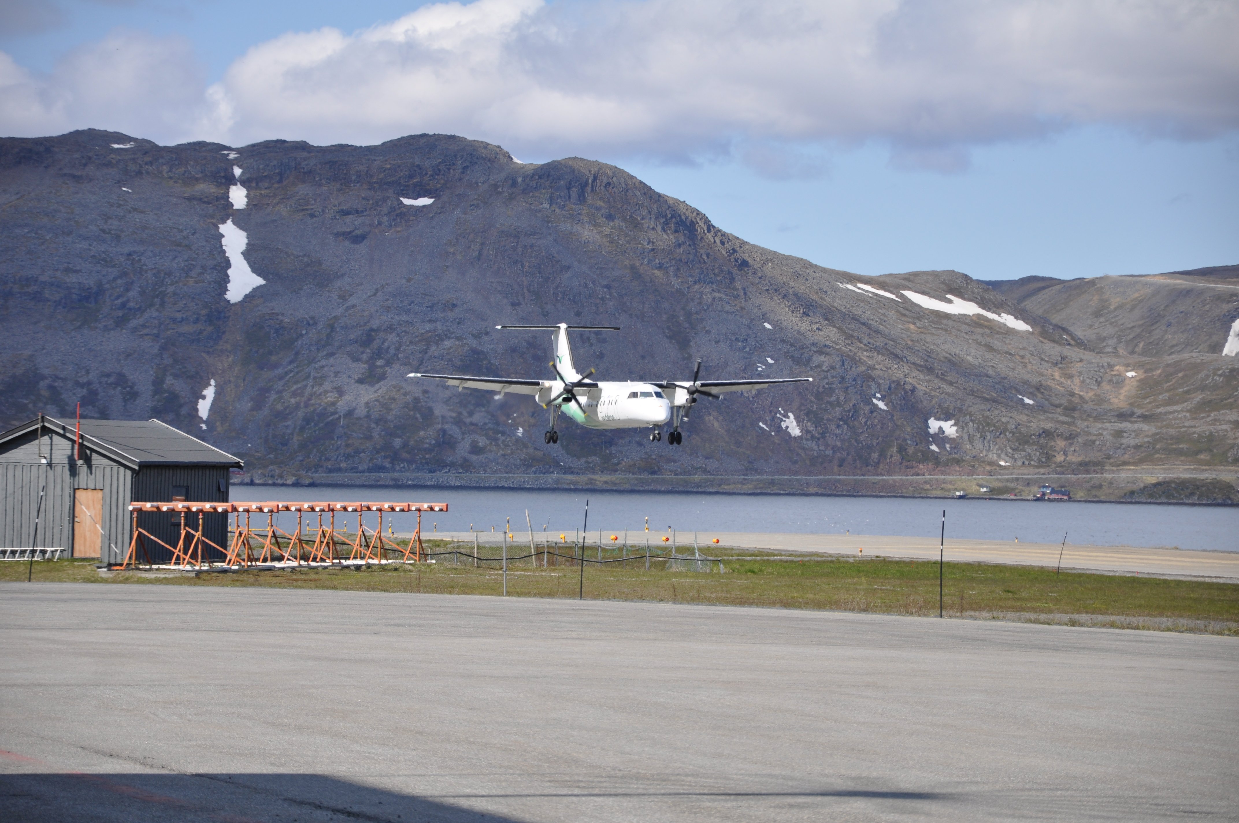 Planes landing at Honningsvåg Airport surrounded by mountain scenery in Norway, with a clear blue sky in the background.