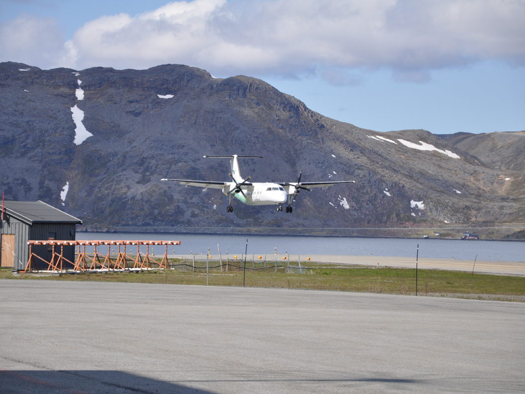 Planes landing at Honningsvåg Airport surrounded by mountain scenery in Norway, with a clear blue sky in the background.
