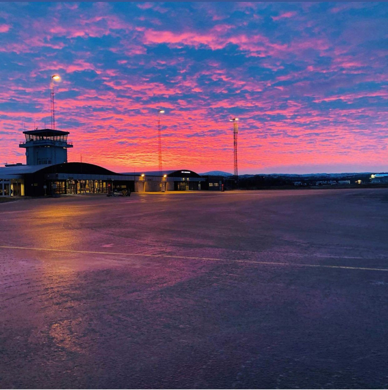 Lakselv flyplass ved solnedgang med fargerik himmel i rosa og blåtonar, terminalbygning og kontrolltårn.