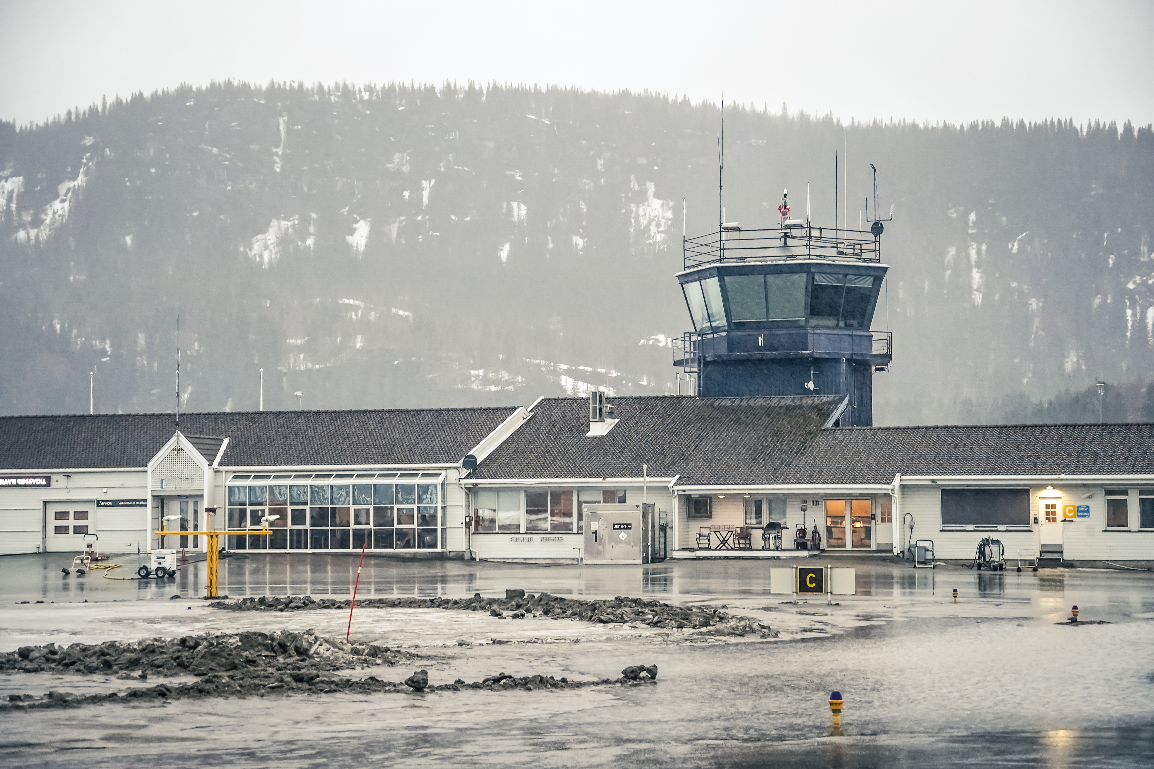 Vinterlandskap ved Mo i Rana flyplass med kontrolltårn, snødekte fjell i bakgrunnen, og oversvømt rullebane.