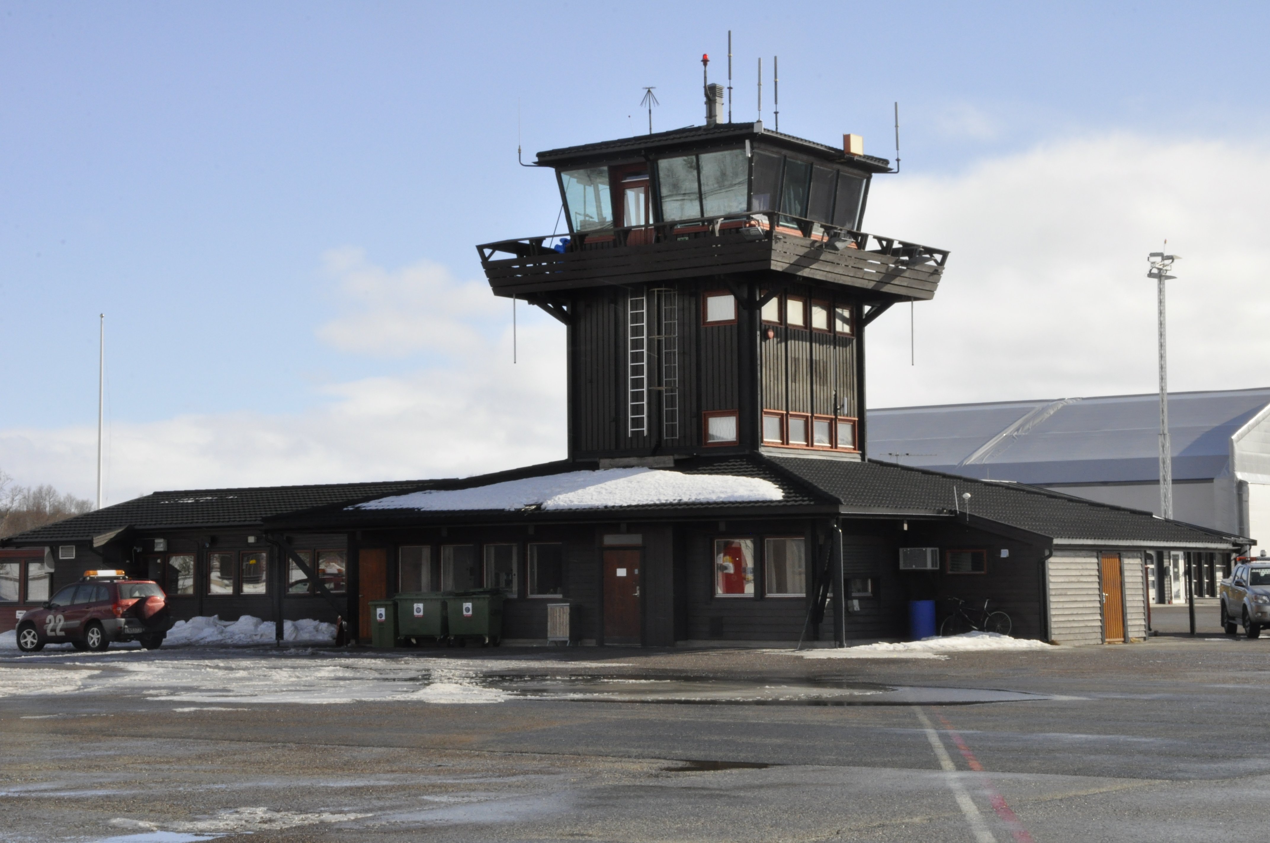 Kontrolltårn ved Røros flyplass med snø på taket, ein parkeringsplass foran og ein bil til venstre. Vinterleg landskap under klar himmel.