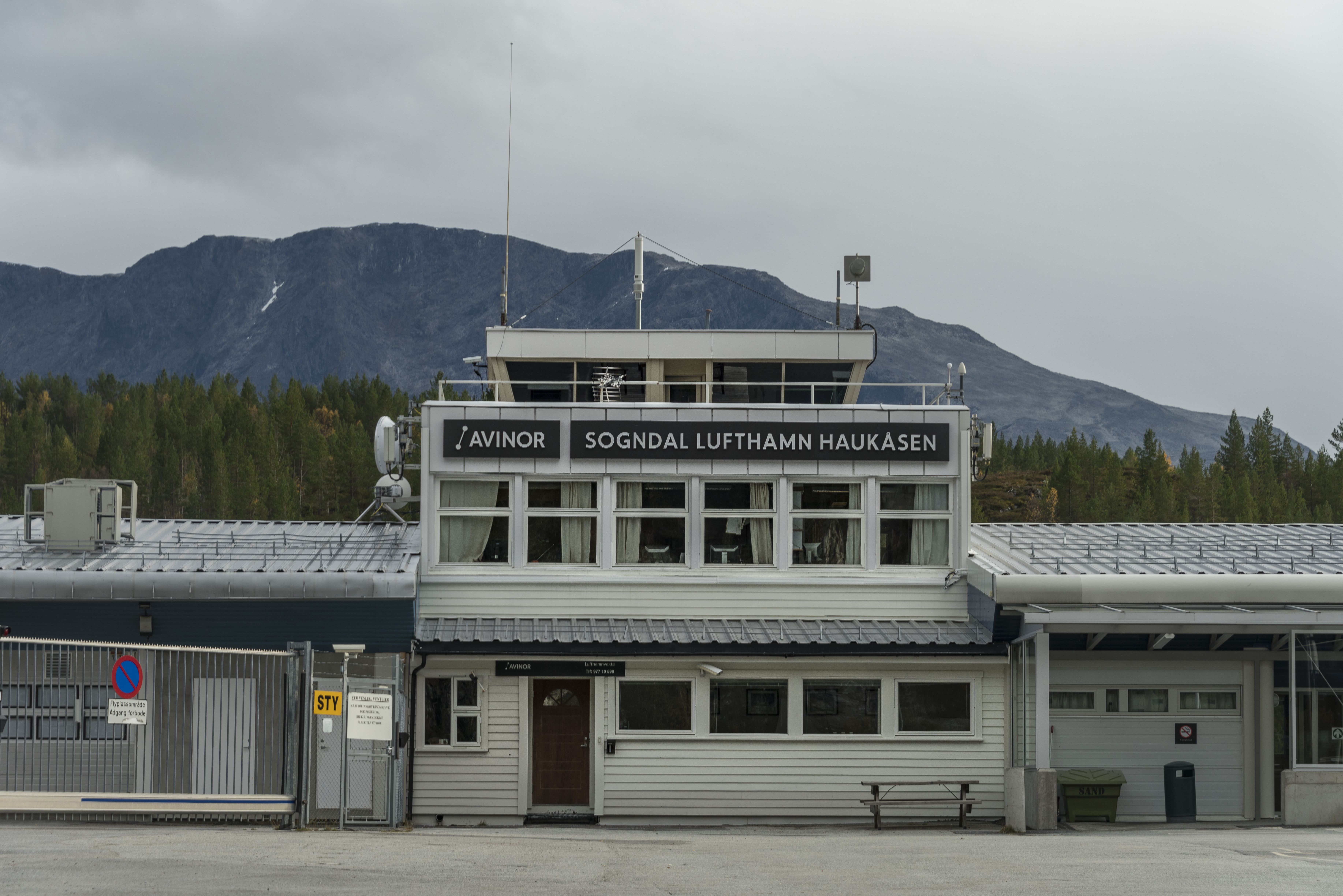 Sogndal lufthavn Haukåsen foran fjellandskap med skog i bakgrunnen, en grå dag.