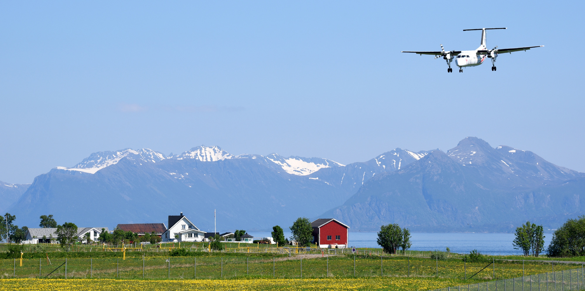 Fly som nærmar seg landingsstripa med fjellandskap i bakgrunnen og norske gardshus i forgrunnen.