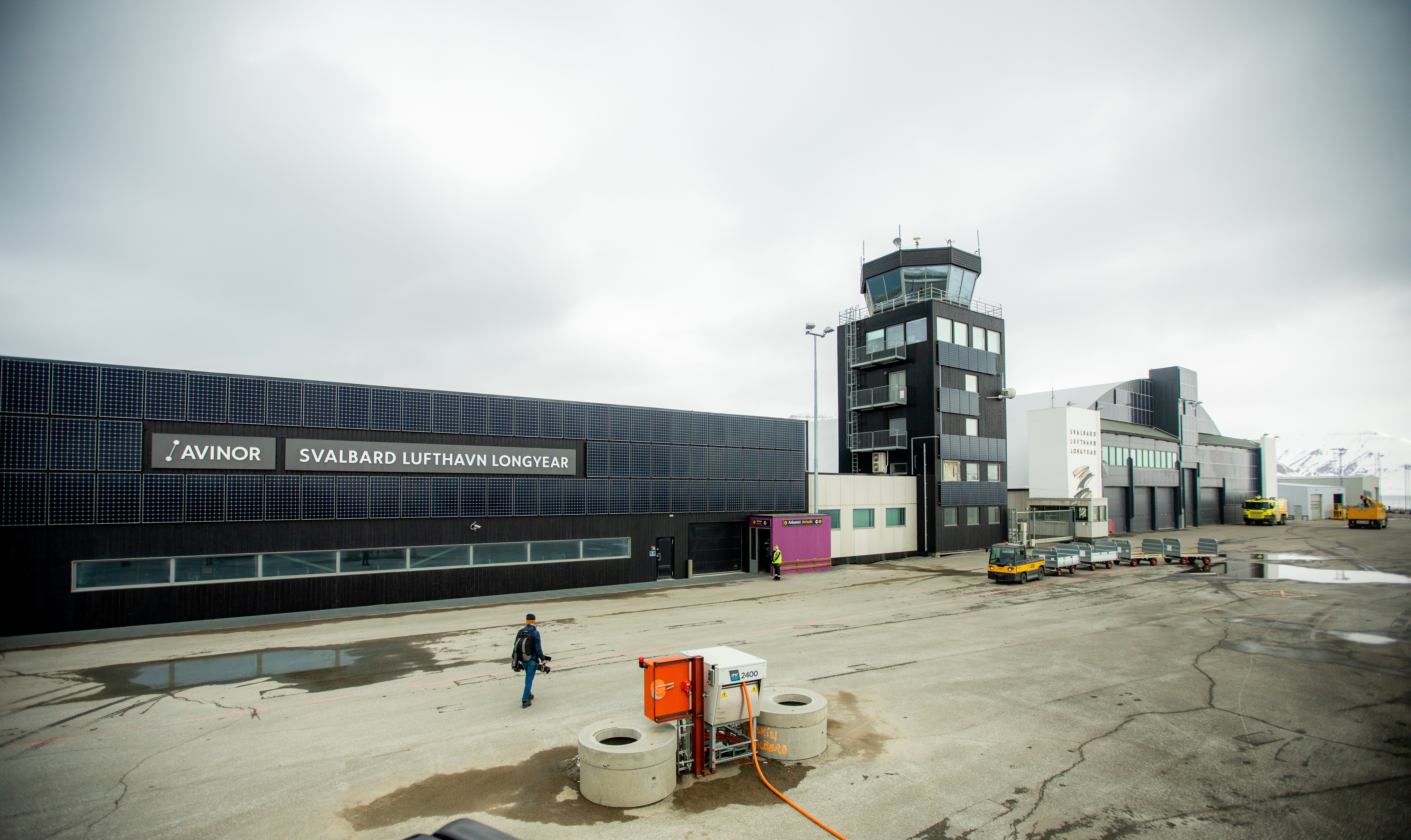 Svalbard Airport in Longyearbyen, with the terminal building and control tower in the foreground, under cloudy weather.