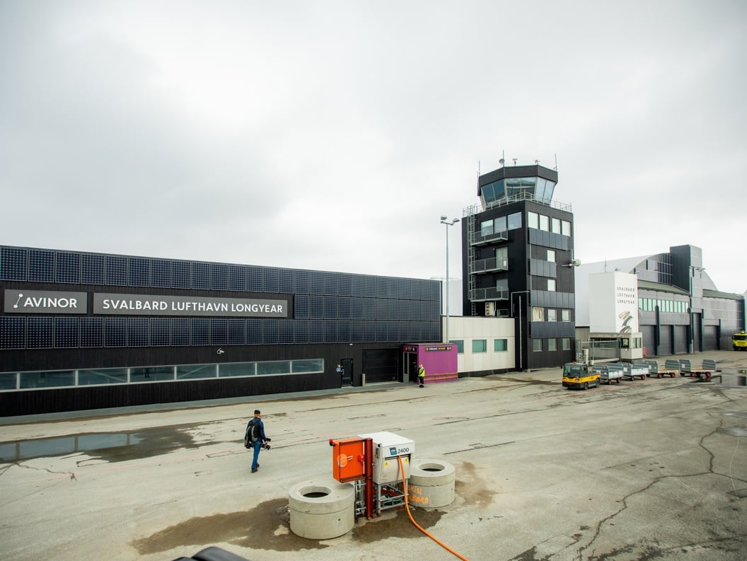 Svalbard lufthavn i Longyearbyen, med terminalbygningen og kontrolltårnet i forgrunnen, under overskyet vær.