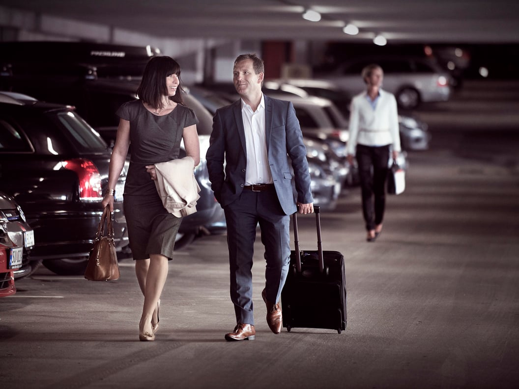 Business people on the move in a parking garage, carrying suitcases and handbags, dressed in formal attire.