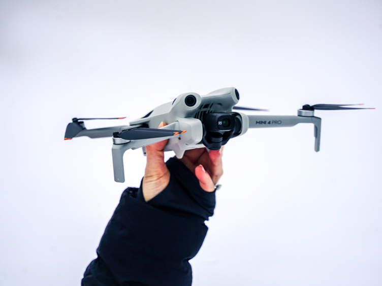 Hånd holder en grå drone av typen Mini 4 Pro mot en hvit bakgrunn, klar for takeoff.